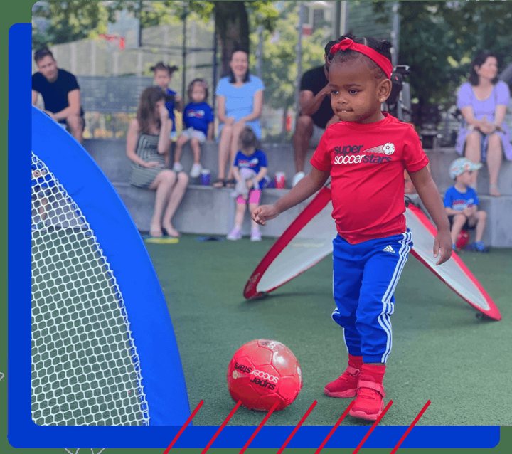 A toddler in a red jersey kicks a ball